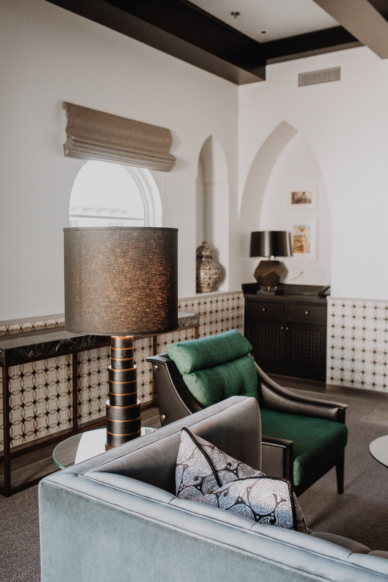 A lobby lounge with a green chair, a blue sofa, and a lamp.
