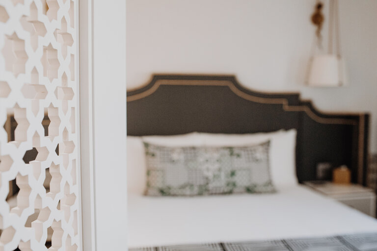 a bed with a dark headboard and white bedding is visible through a doorway with a decorative partition