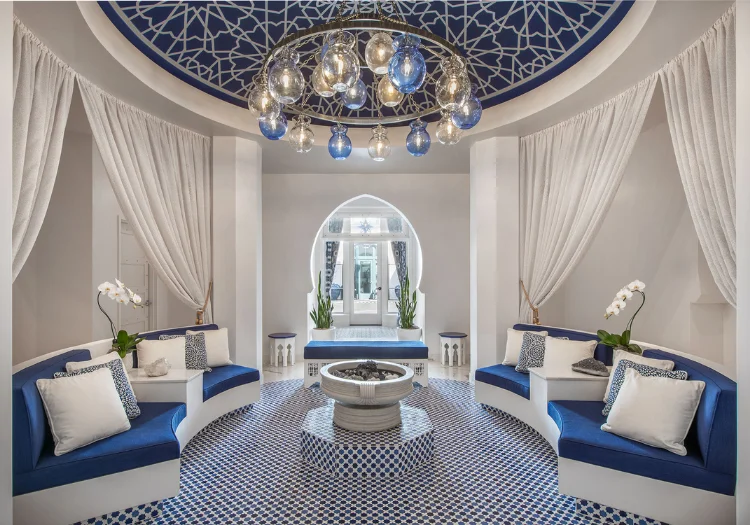A luxurious lounge with blue and white decor, a fire pit, and a chandelier.