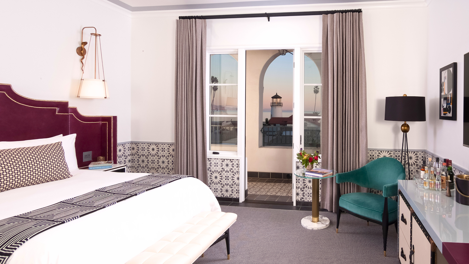 A luxurious hotel room with a large bed, a chair, and a table with a view of a lighthouse outside the window.